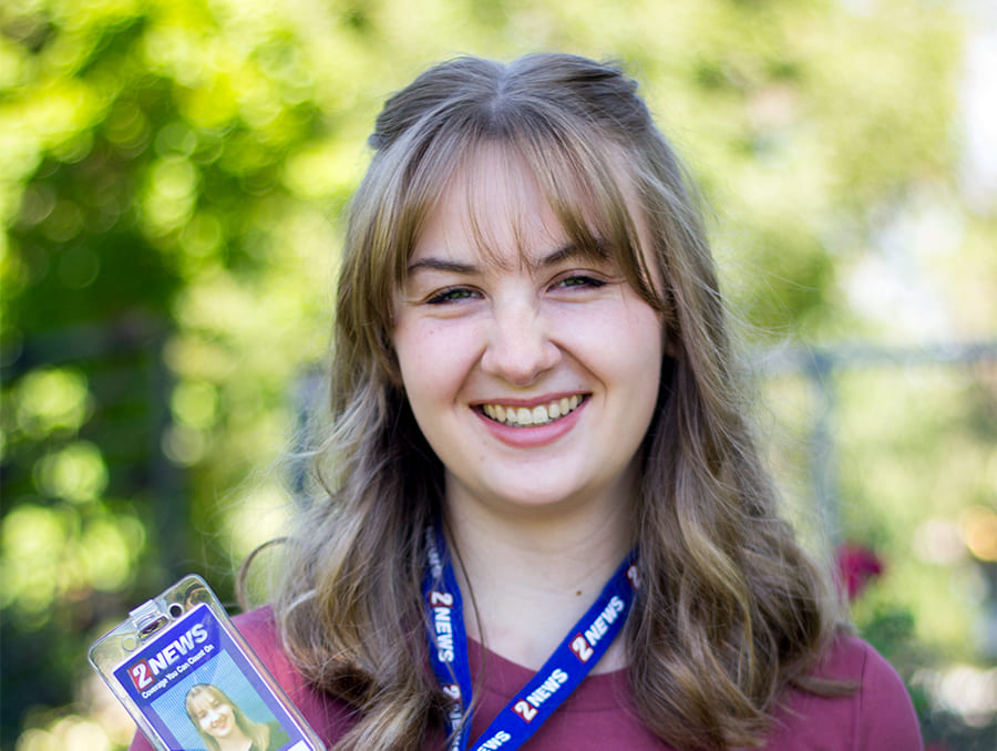 Chloe Cross smiles and holds up a pass that says 2NEWS.