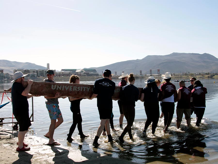 14 students carrying a canoe into the water at the Sparks Marina.