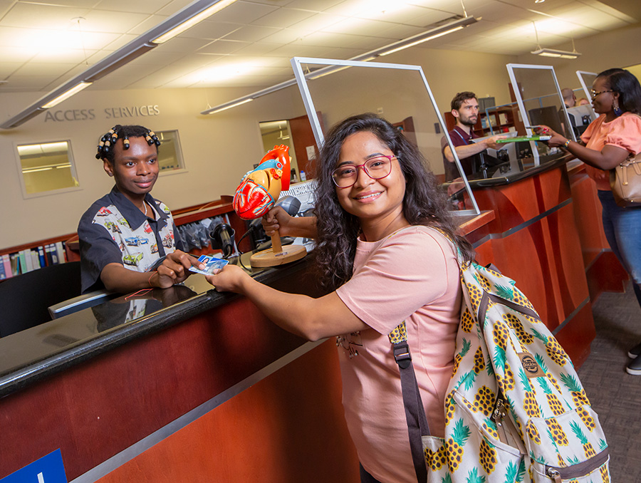 Two Libraries student assistants pass two library users their checked-out library materials at the University Libraries access services desk located inside the Mathewson-IGT Knowledge Center.