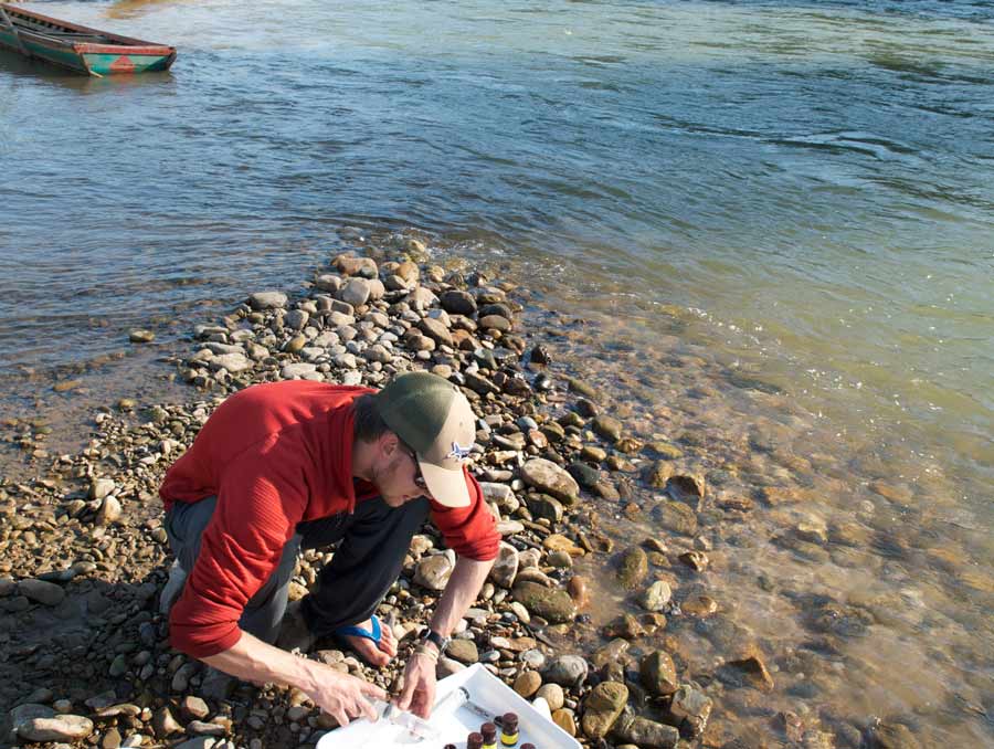 Aaron Konig kneels on a riverbank preparing scientific samples.