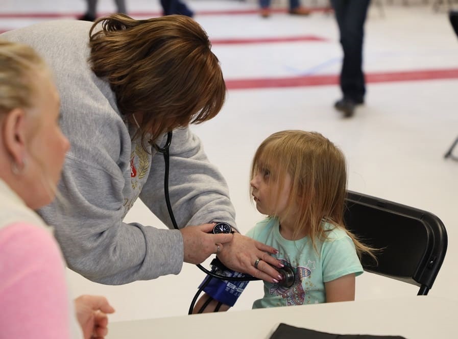 A child from Tonopah gets a medical exam by a woman who is checking vitals.