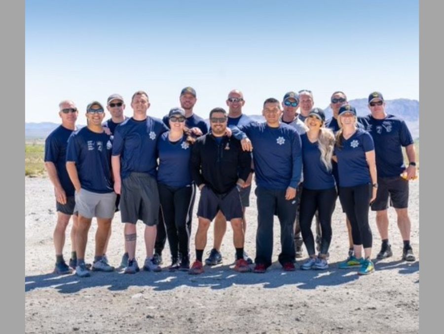 A group of men and women stand smiling for the camera outside dressed in running police branded gear.