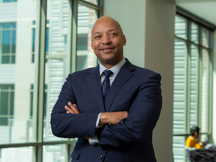 Man in a suit with arms crossed standing indoors.