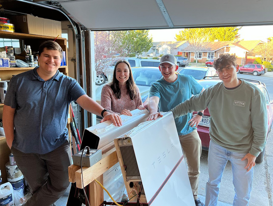 Four students standing in a residential garage with a Tesla Powerwall battery.