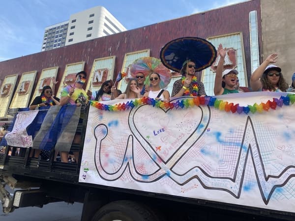 10 people standing on a float waving and smiling at the camera in the parade