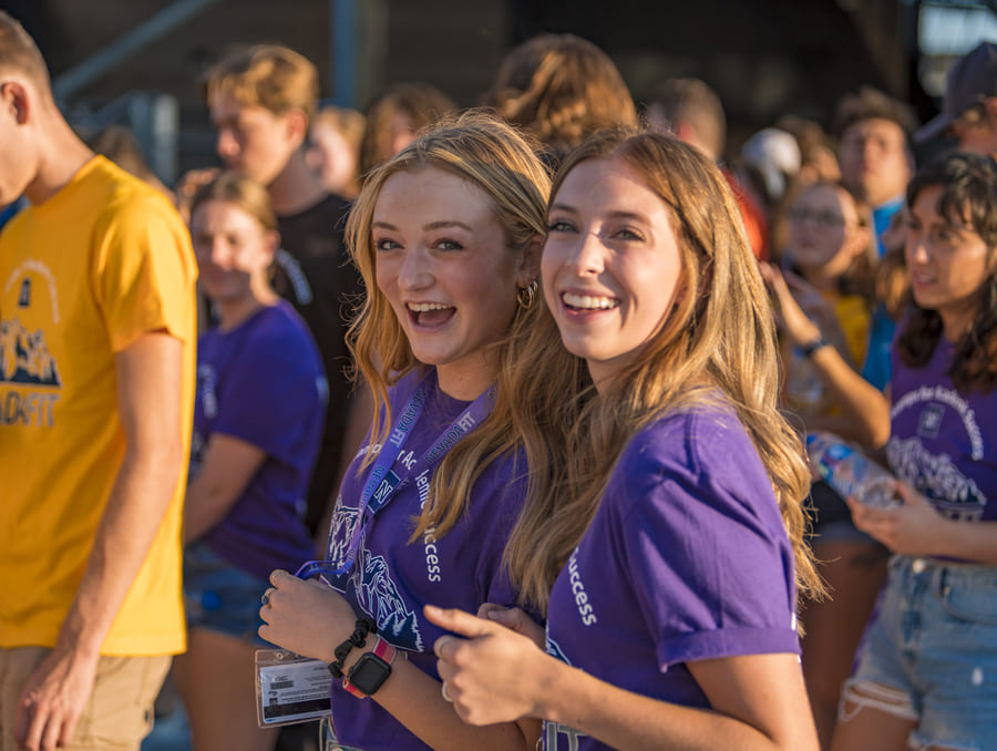 Two students dressed in purple smile at the camera from a crowd of students in all different colored t-shirts during the opening ceremony of NevadaFIT.