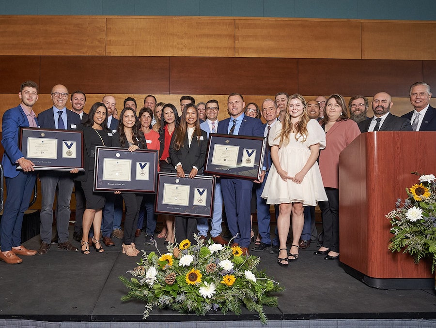 26 students posing with Dean Mosier and framed awards at the EMBA graduation ceremony