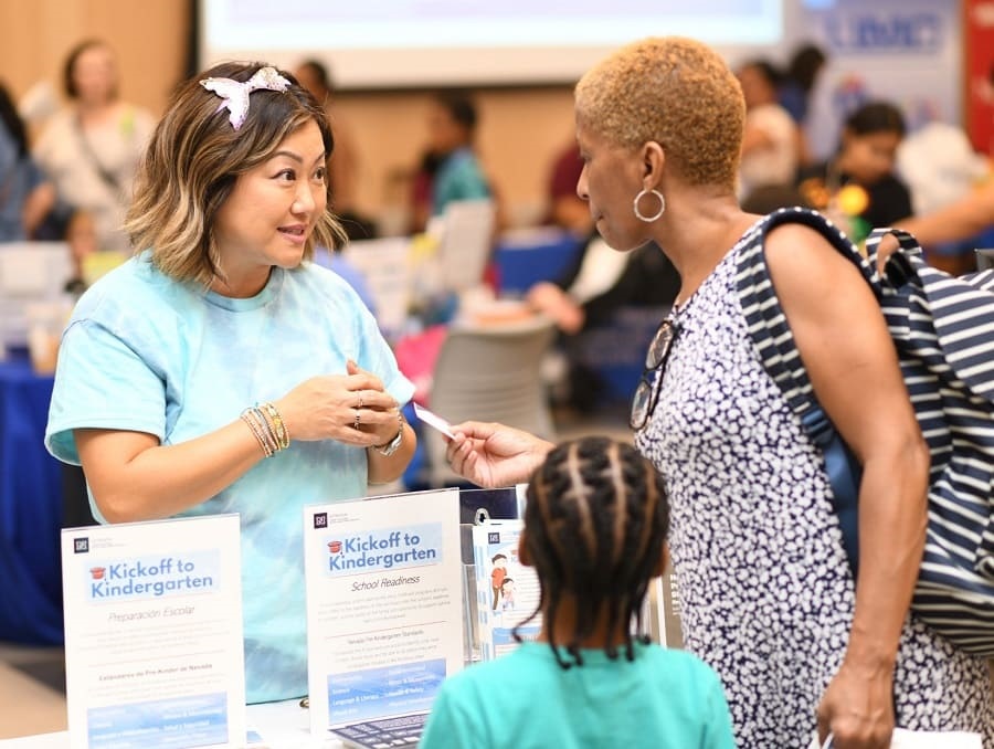 A parent and child being welcomed to the event while holding a handout from an Extension Staff. 