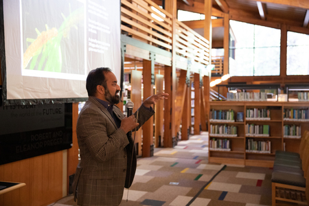 Dr. Sudeep Chandra stands in front of a projection screen talking into a microphone