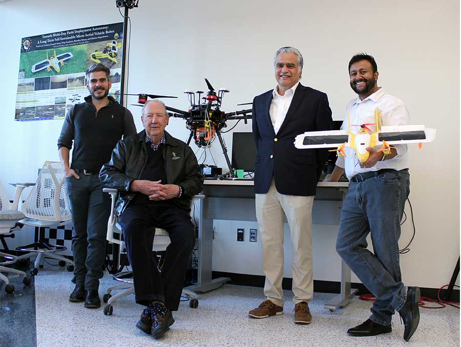 Christos Papachristos; Tom Hall (seated); Petros Voulgaris; and Aditya Nair (holding a drone) pose inside Papacristos' lab. 