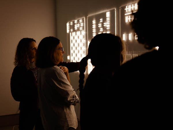 A group of people looking at and analyzing Choey's artwork while standing directly in front of the piece.