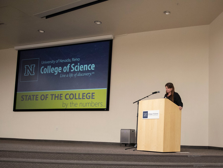 Louisa Hope-Weeks stands at a podium with a large screen behind her.