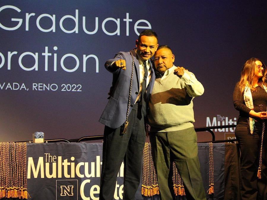 A graduate and a loved one hug and make a fist sign toward the camera while smiling broadly on stage during the Unity Graduation Celebration 2022.