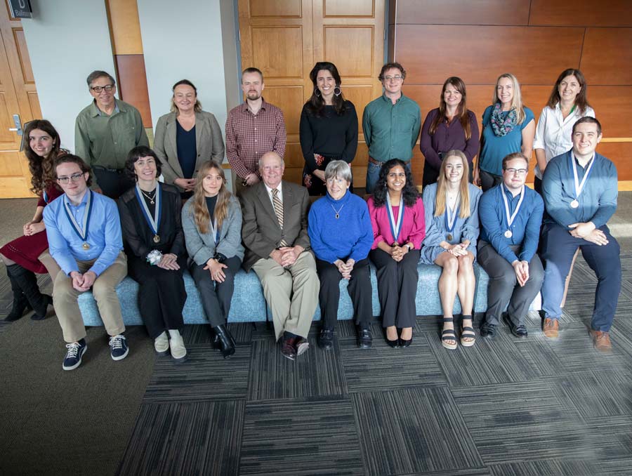 A group of people sit on or stand behind couches and smile for a photo.