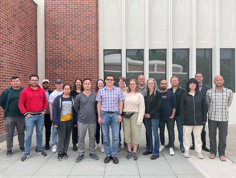 A group of 18 people stands in front of the physics building.