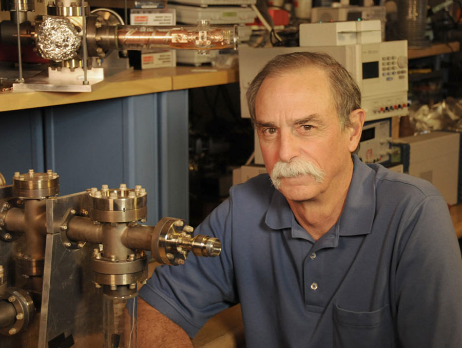 A man sits in a laboratory next to a metal device.