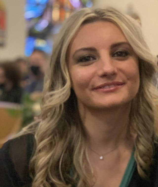 Woman smiling in a black shirt with a green accent detail collar.