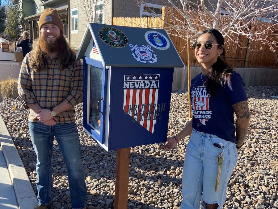 Man and woman standing on either side of a box that is painted blue and decorated with the state of Nevada with red and white stripes inside. 