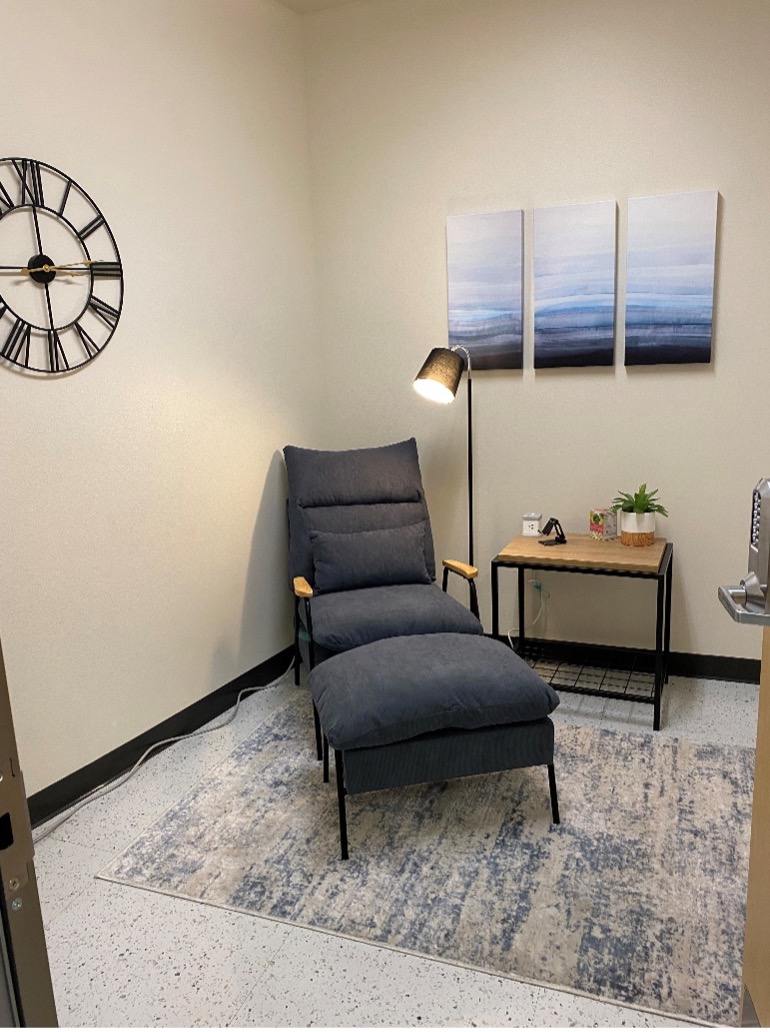 A cozy room with a chaise lounge chair with a side table and a lamp.