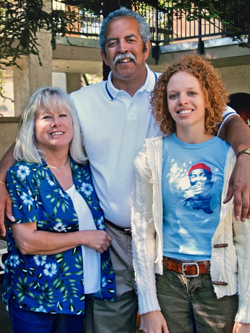 Michael and wife Suzanne stand smiling with their arms around a young woman, their daughter, Jena. 