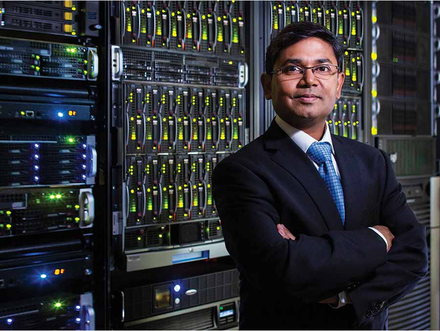 Shamik Sengupta, shown from the waist up, standing in front of a wall of computer servers.