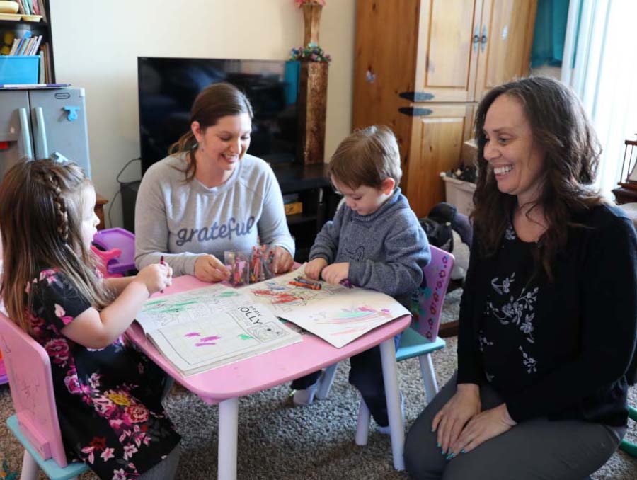 Home visitor Candy Cannon (right) sits at a table with a mother and her two children as the children color.