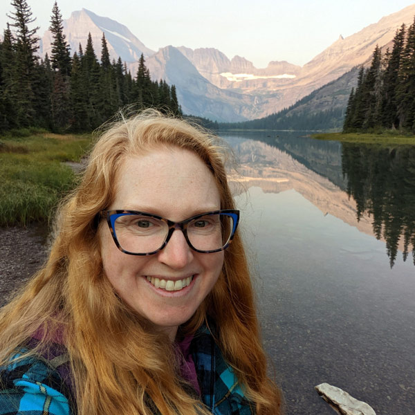 Rachel MIcander smiles in front of an alpine lake.