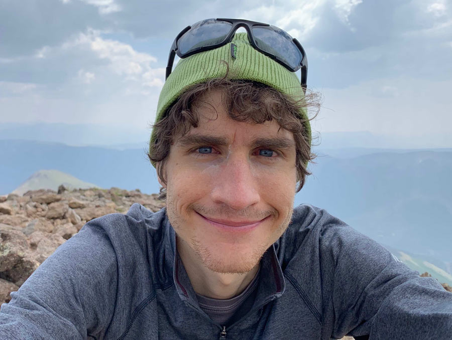 Daniel Trugman smiles in a selfie on a mountaintop. He is wearing a green beanie.