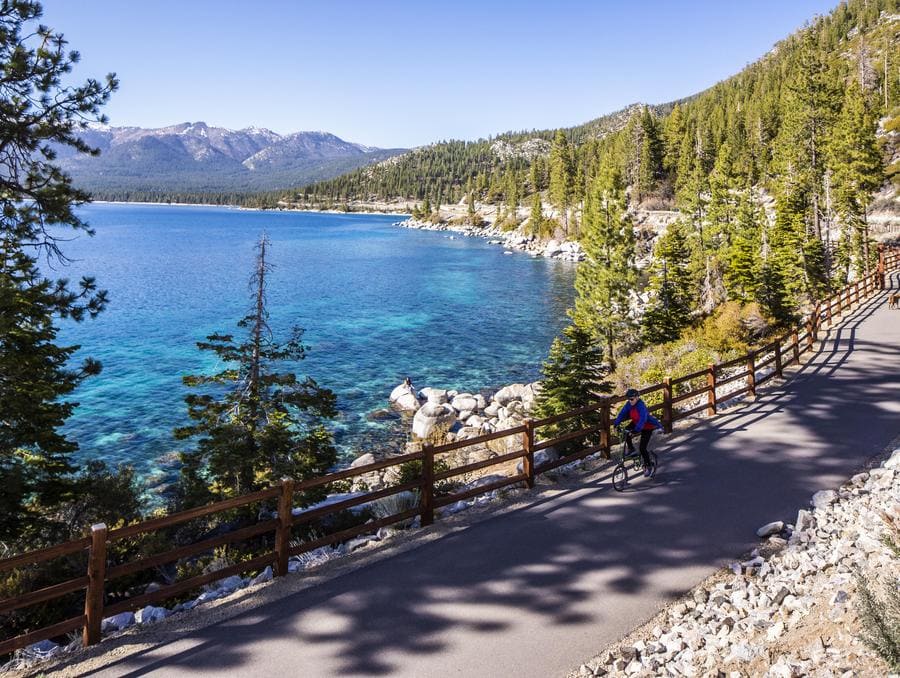 The walkway and sidewalk that stretches across Lake Tahoe's shoreline with a biker and a dog walker on it.