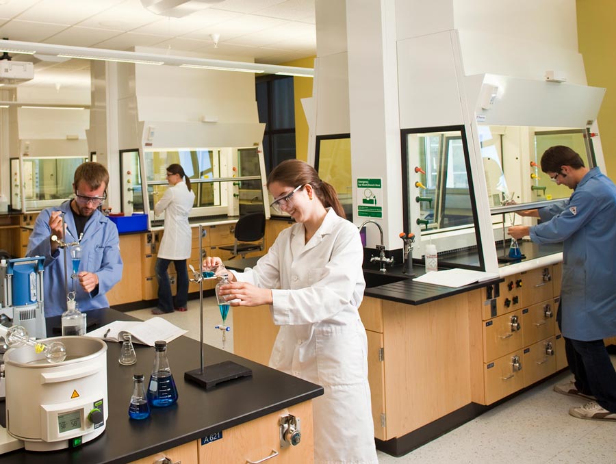People in a chemistry lab wear lab coats and safety goggles as they mix chemicals.