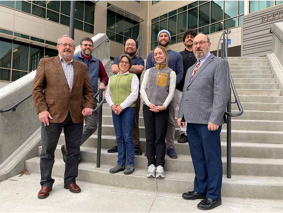 Seven people wearing casual business attire standing on the steps outside of the William Pennington Engineering Building.