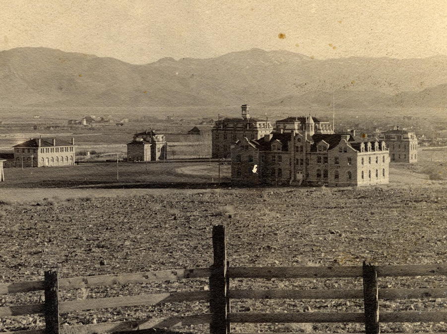 The UNR campus from the early 1900s in sepia tones. It is mostly an empty field with Morrill hall and buildings from the university quad visible.