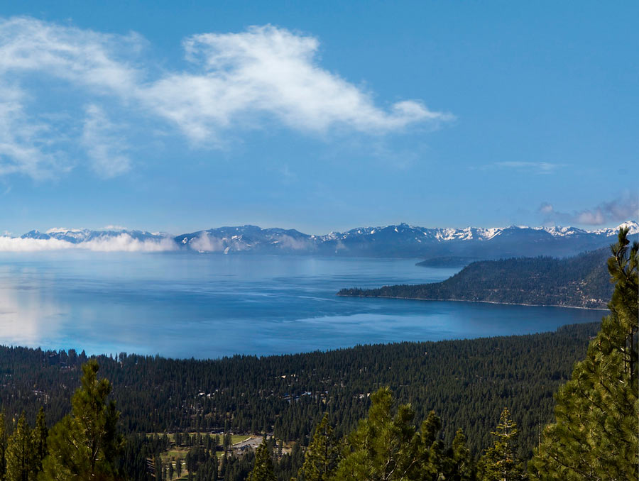 Overlooking Lake Tahoe on a fairly sunny day with several clouds in the sky.