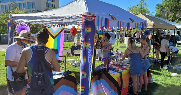 People interacting with the staff and students at the Orvis School of Nursing booth at Northern Nevada Pride 2022 decorated with pride flags and rainbows