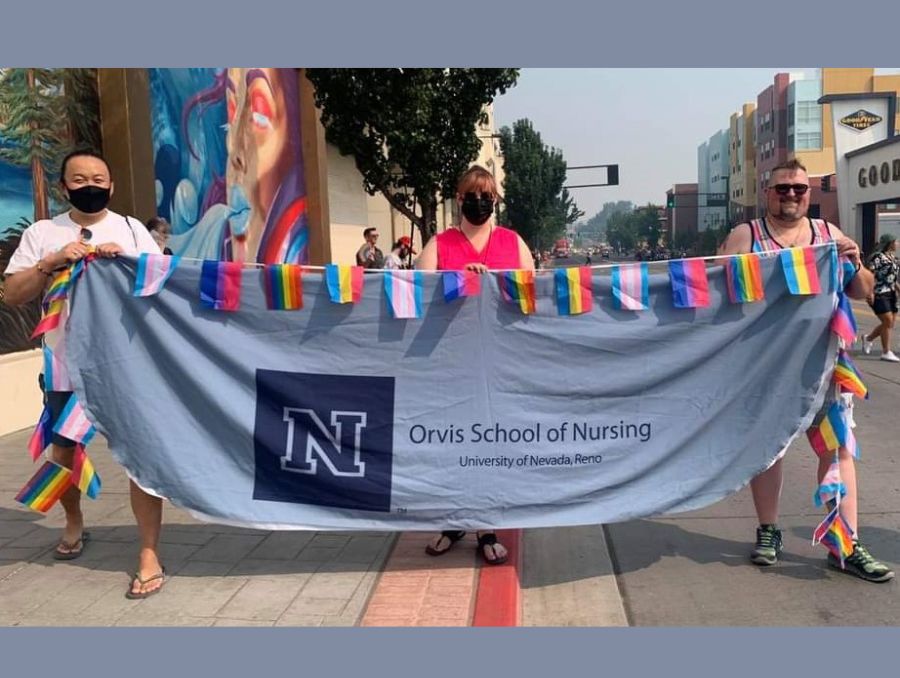 University staff and students hold up banner for Orvis School of Nursing decorated with pride flags at Northern Nevada Pride 2021