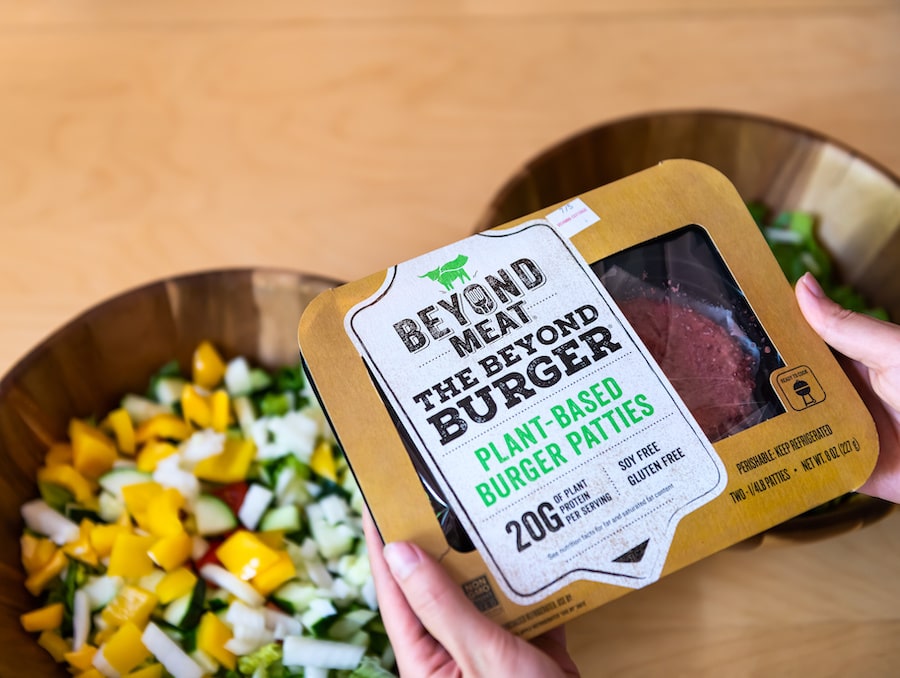 a pair of hands holding up a package of Beyond Meat over a bowl filled with chopped vegetables
