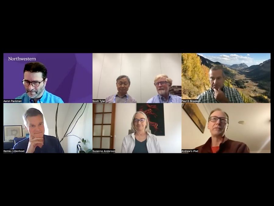 A screengrab from a video recording of a Zoom meeting. There are 7 participants in the Zoom meeting on 6 screens. Two men share a screen in the middle.