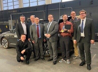A group of conference participants pose in front of an autonomous vehicle