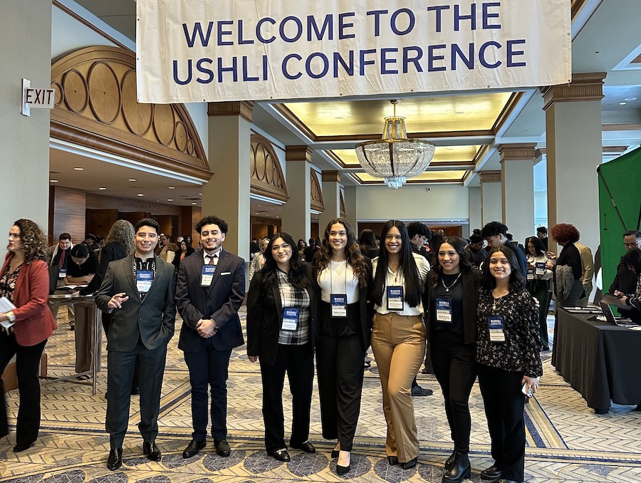 Seven students pose in front of a banner that reads "Welcome to the USHLI Conference"