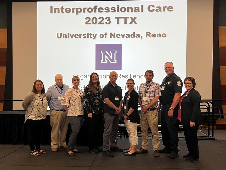 A group of nine smiling people posing for the camera at the Interprofessional Care 2023 TTX Training Exercise