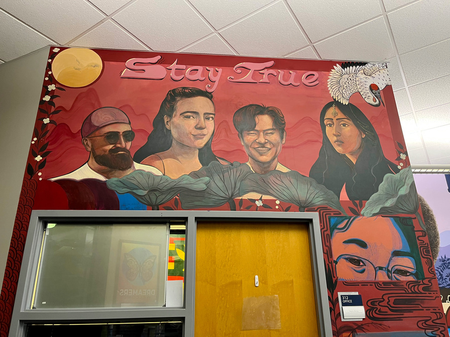 AAPI mural in the Multicultural Center depicting four smiling people of AAPI heritage with the words "Stay True" above them and a full moon in one corner and a bird in the other corner.