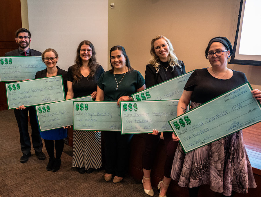 6 individuals hold extra large, green checks for winning the 3-minute thesis competition in 2022. 