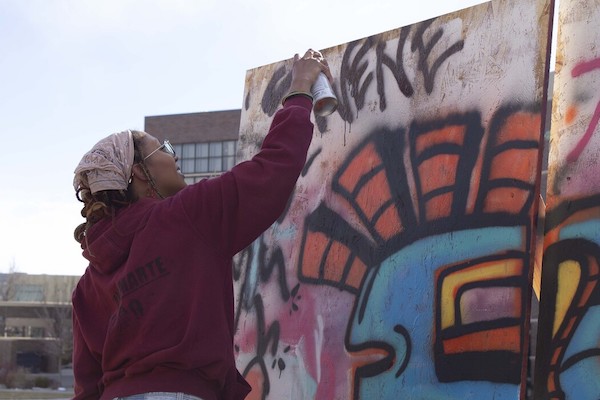 Student Serene Townsell spray paints the top of the collaborative graffiti freewall. 