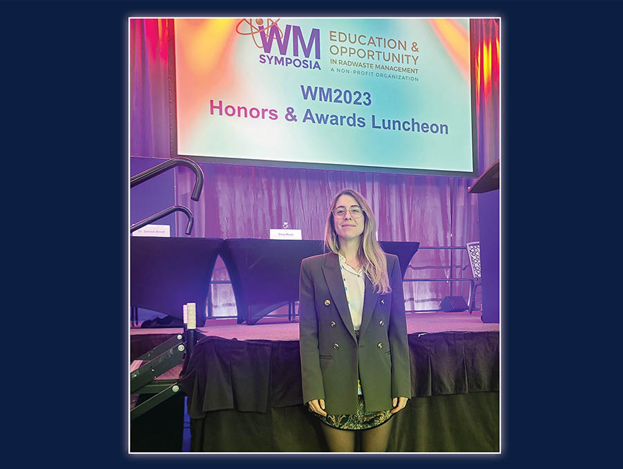 Lucia Poole standing indoors in front of a sign announcing the WM Symposia 2023 honors and awards luncheon
