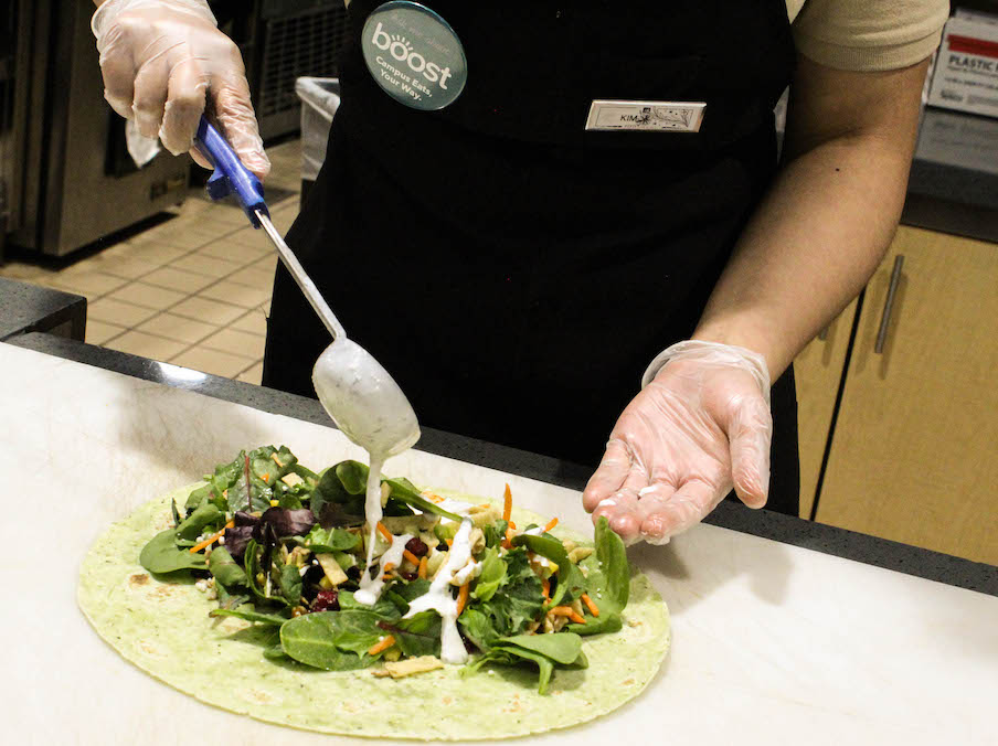 A salad wrap being prepared with fresh ingredients by someone who is wearing gloves.