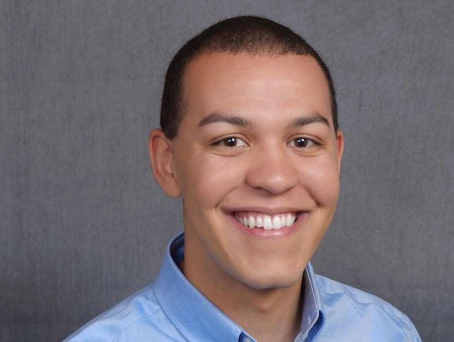 Man in blue collared shirt with a plain grey background. 