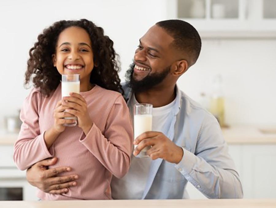 A father and daughter in the kitchen together, smiling and enjoying glasses of milk.