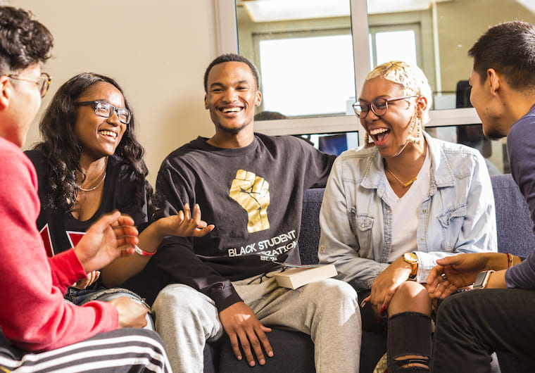 Group of people laughing and talking together in front of a white wall with glass windows. 