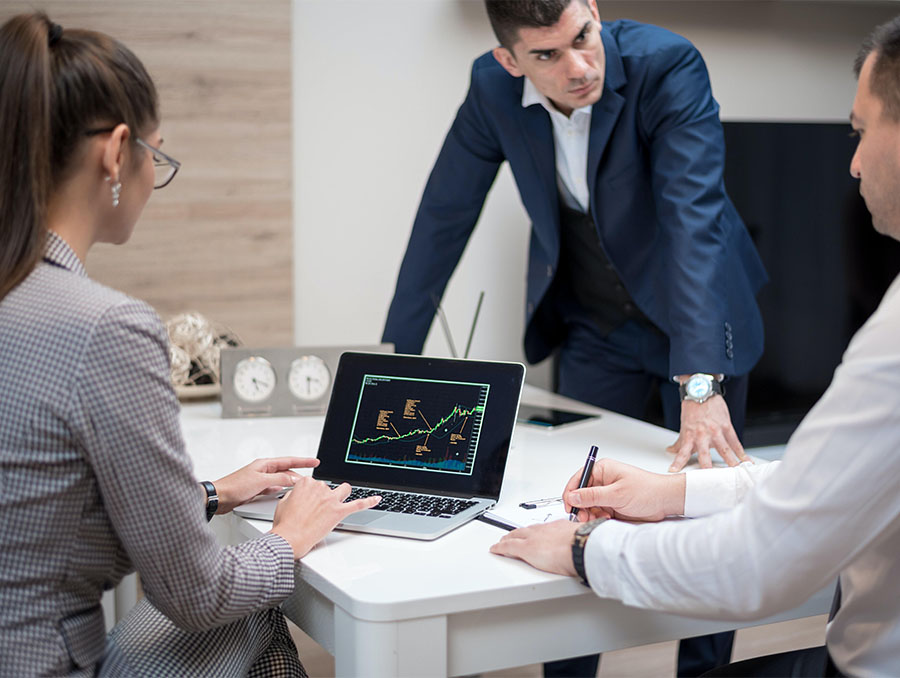 Two men and one woman dressed in business attire surround an open laptop