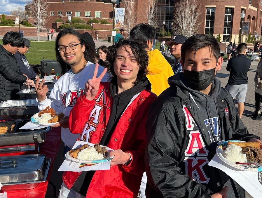 Three students stand outside with plates of food at the API Night Market on campus at UNR.